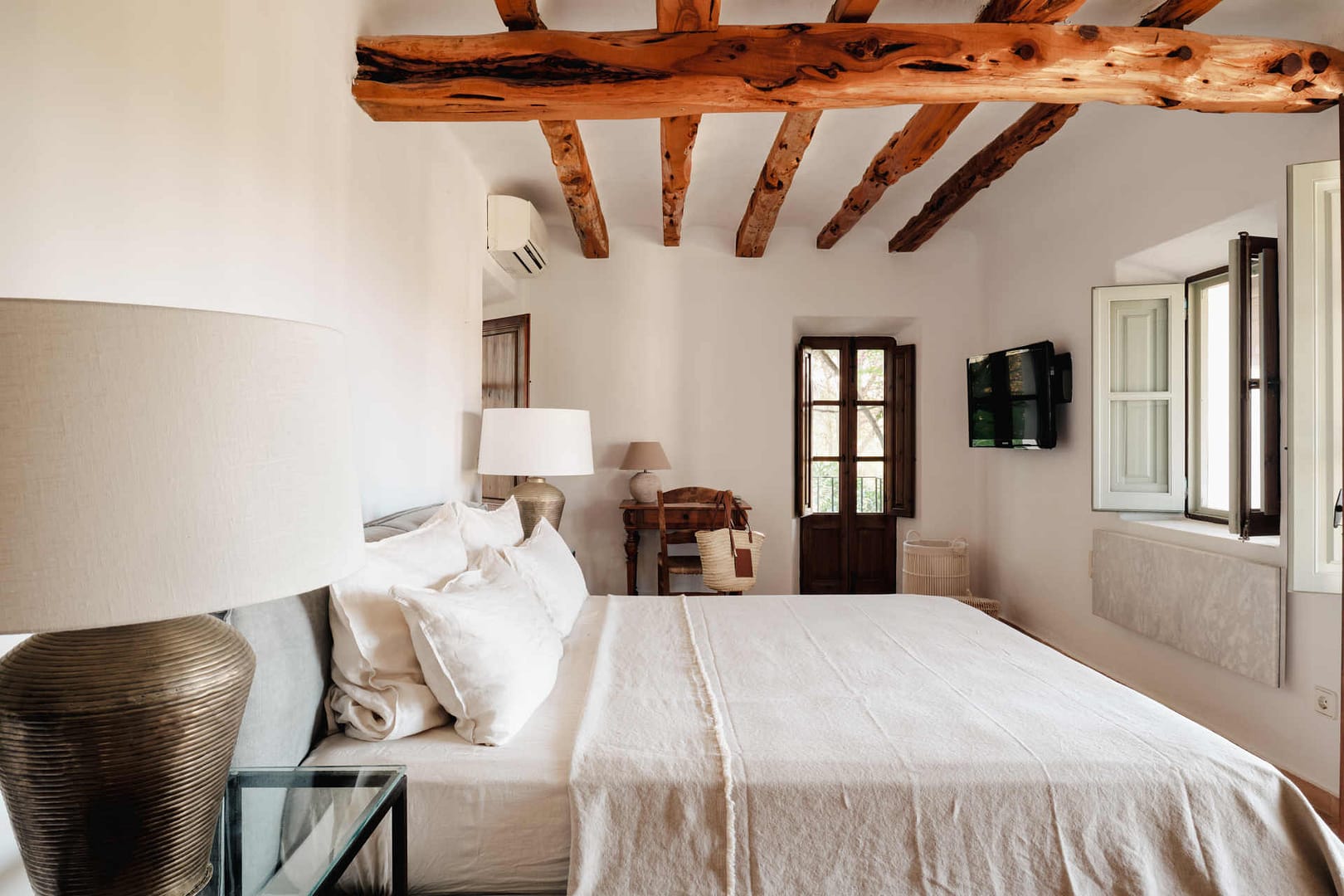 Helles Schlafzimmer im Gästehaus einer Ibiza-Finca mit großen Fenstern, Holzbalken und gemütlichem Bett