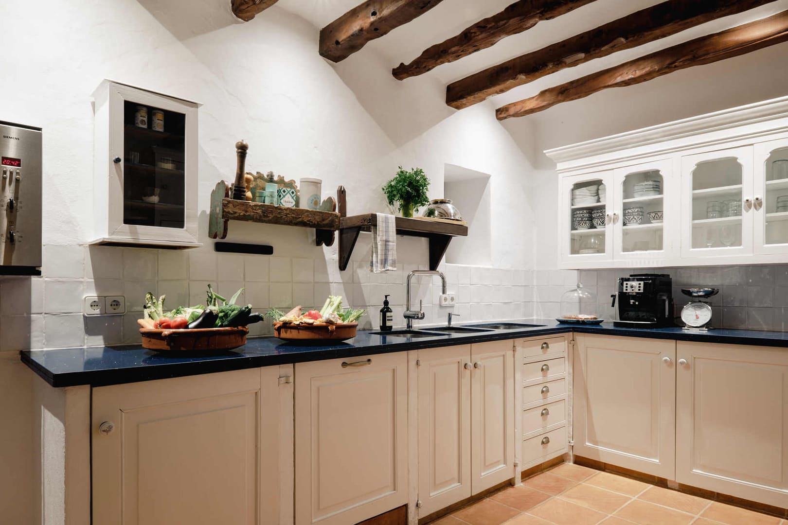 Helle Küche in einer Finca auf Ibiza mit blauer Arbeitsplatte, weißen Schränken und frischem Gemüse auf der Arbeitsfläche