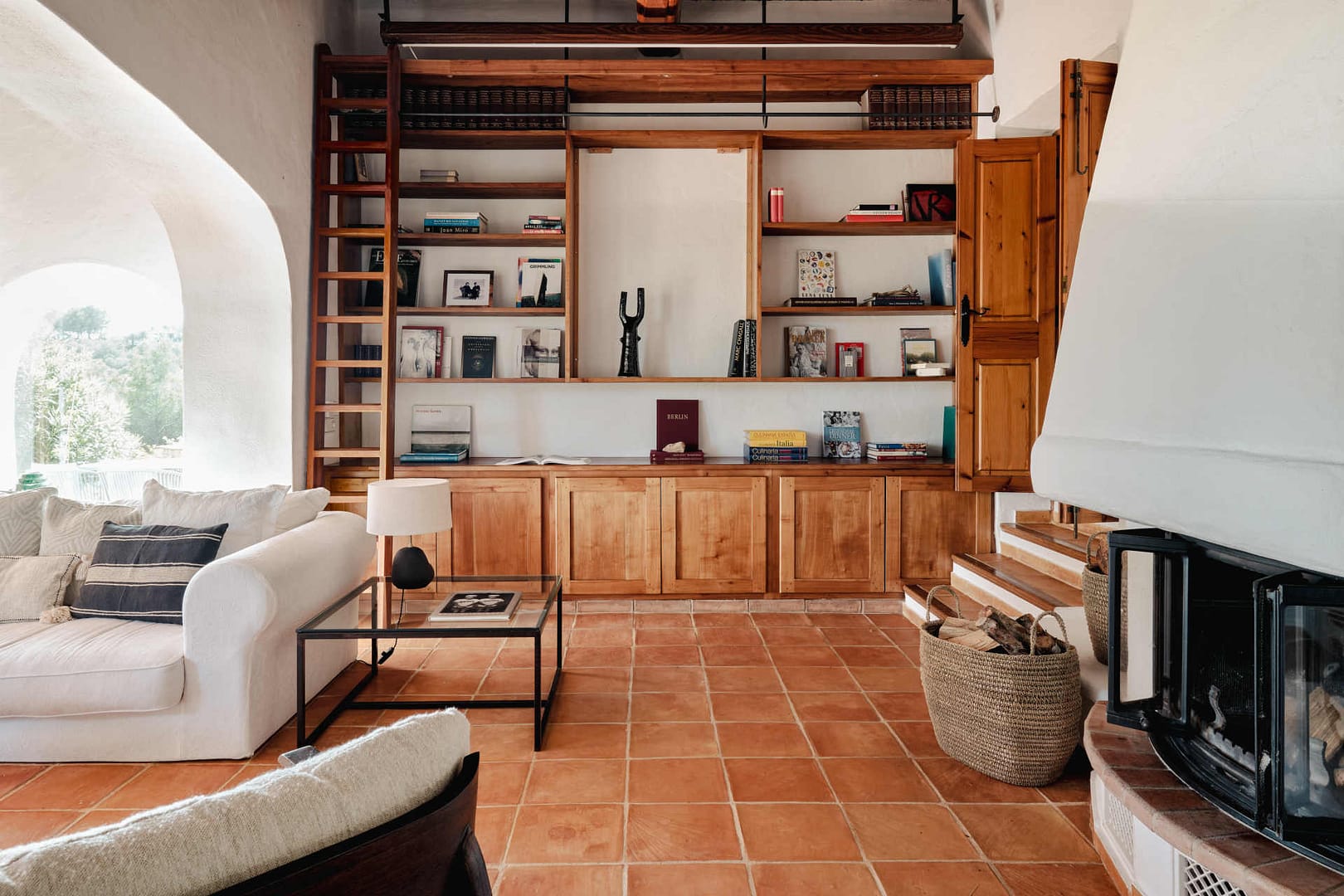 Helles Wohnzimmer in einer Finca auf Ibiza mit großem Holzbücherregal, Kamin und weißen Sofas