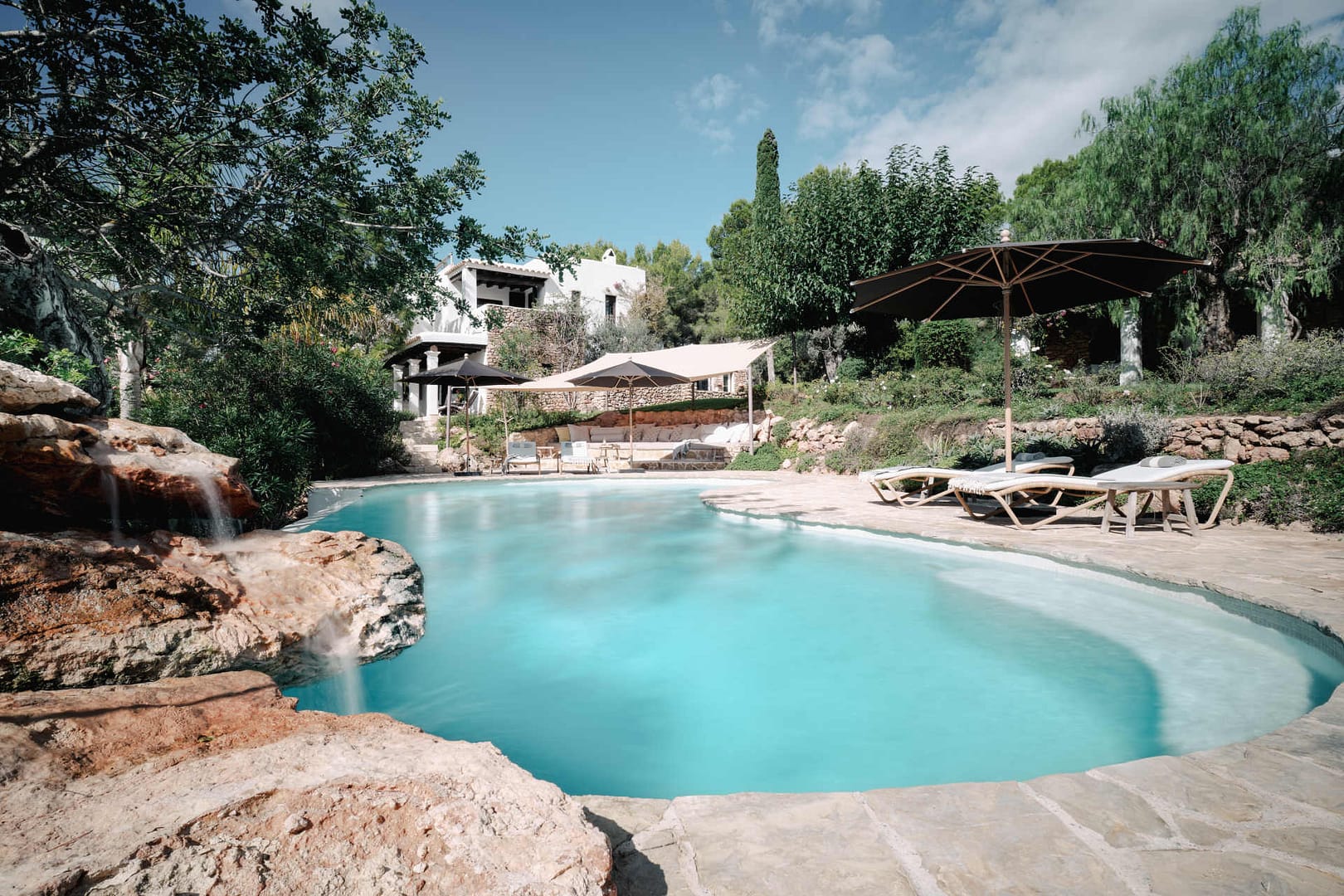 Freiform-Pool mit natürlicher Steinumrandung, Sonnenschirmen und Liegen in einem mediterranen Garten