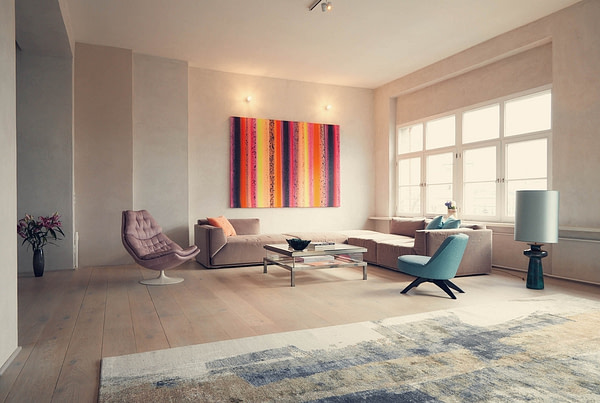 Ein Wohnzimmer mit Sitzecke, mit Sicht auf eine Fensterfront und ein farbenfrohes Kunstwerk