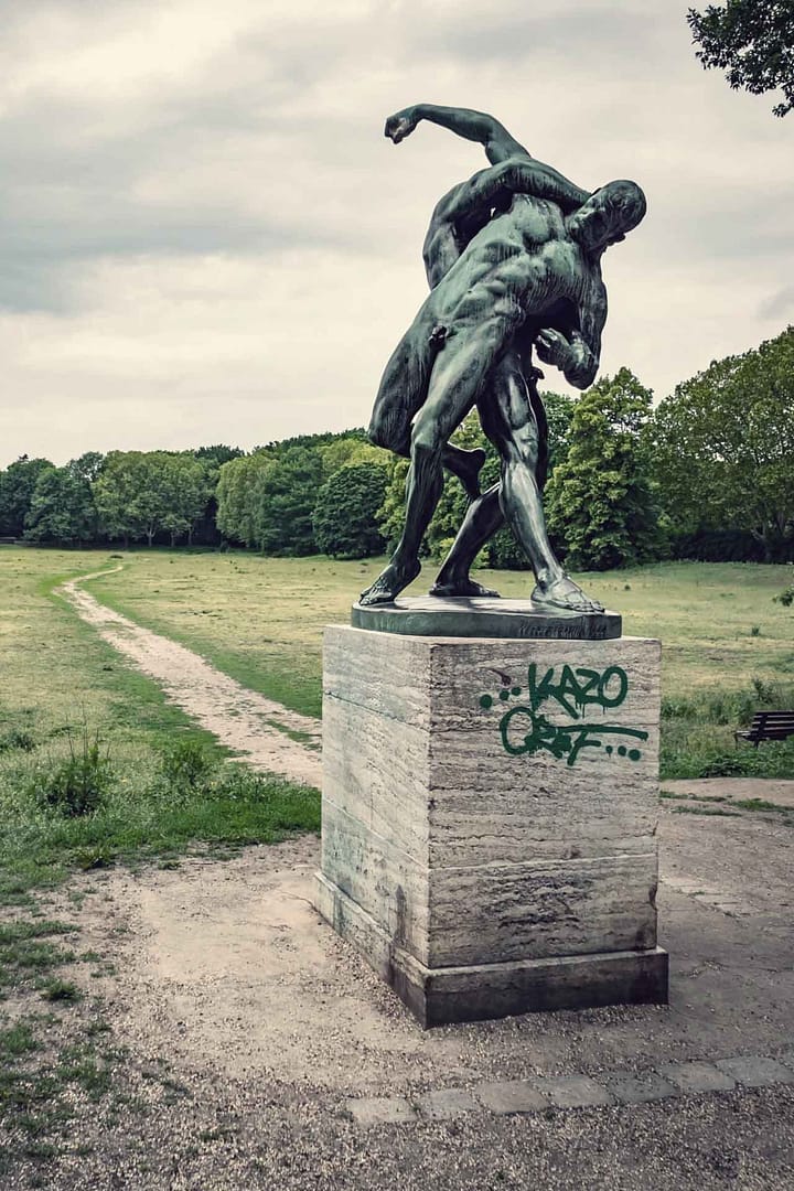 Skulptur zweier kämpfender Männer auf einem Steinsockel im Park Rehberge, Berlin Wedding