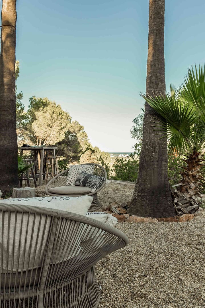 Außenbereich einer Finca auf Ibiza mit zwei modernen Loungesesseln, Kieselboden und Palmen