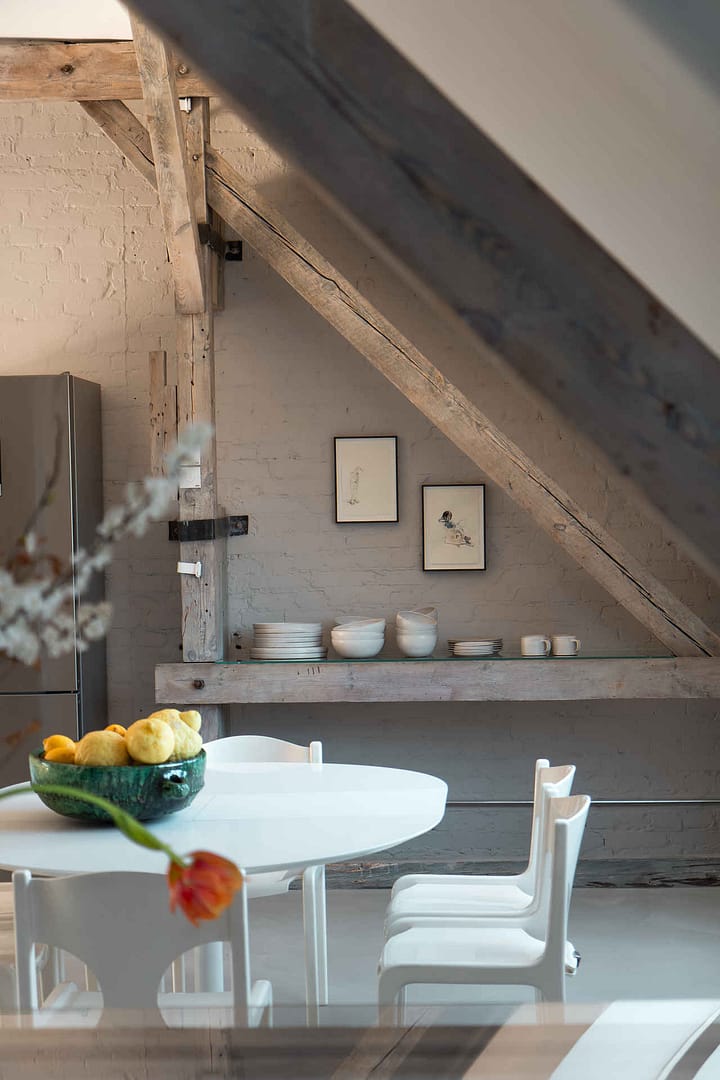 Weißer Esstisch mit Stühlen und Obstschale vor einem offenen Regal mit Geschirr