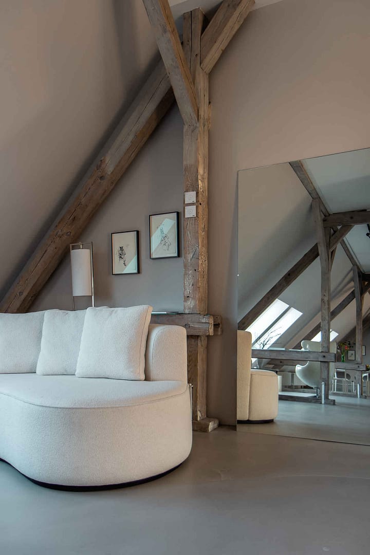 weißes Sofa vor Holzträgern und großem Spiegel in Dachgeschosswohnung