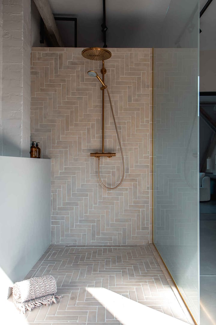 Design Studio Berlin – begehbare Dusche mit Fischgrätfliesen und goldener Armatur