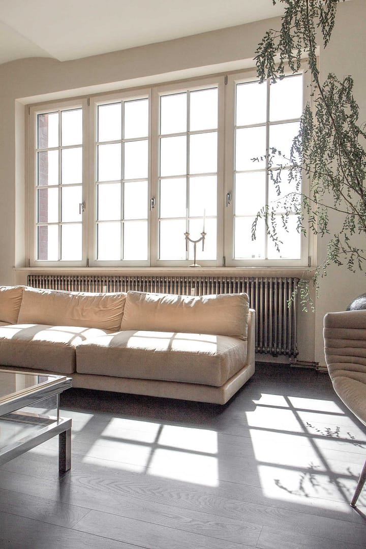 sonnendurchflutetes Wohnzimmer mit beigefarbenem Sofa und großen Sprossenfenstern