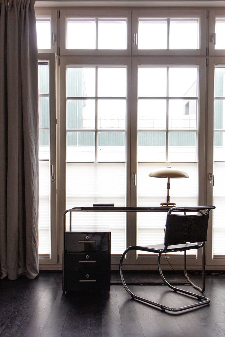Schreibtisch mit Designstuhl und Tischlampe vor bodentiefem Fenster