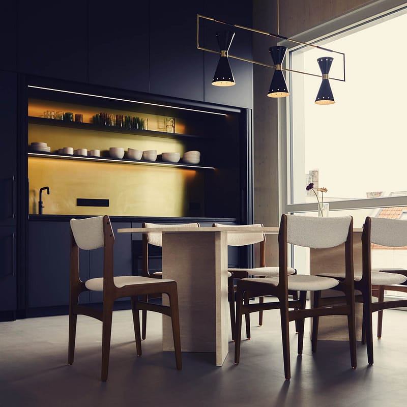 Moderner Essbereich mit ovalem Tisch und sechs gepolsterten Stühlen vor einer Küchenwand mit versteckten Schränken und offenen Regalen, helle Fensterfront im Hintergrund.